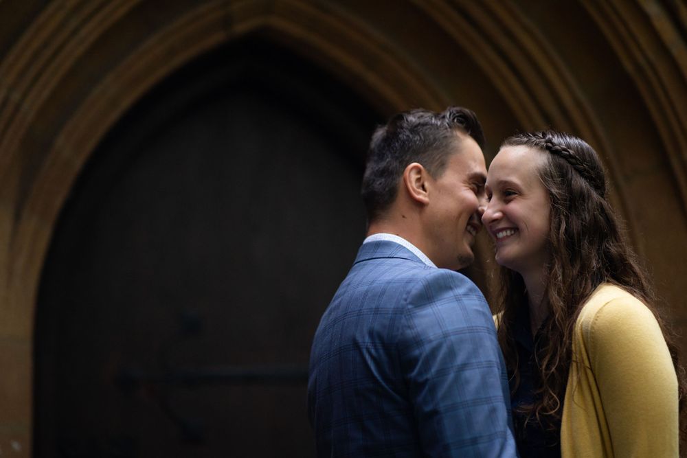 Romantic moment captured between couple in a blue suit and yellow top beneath gothic architecture.