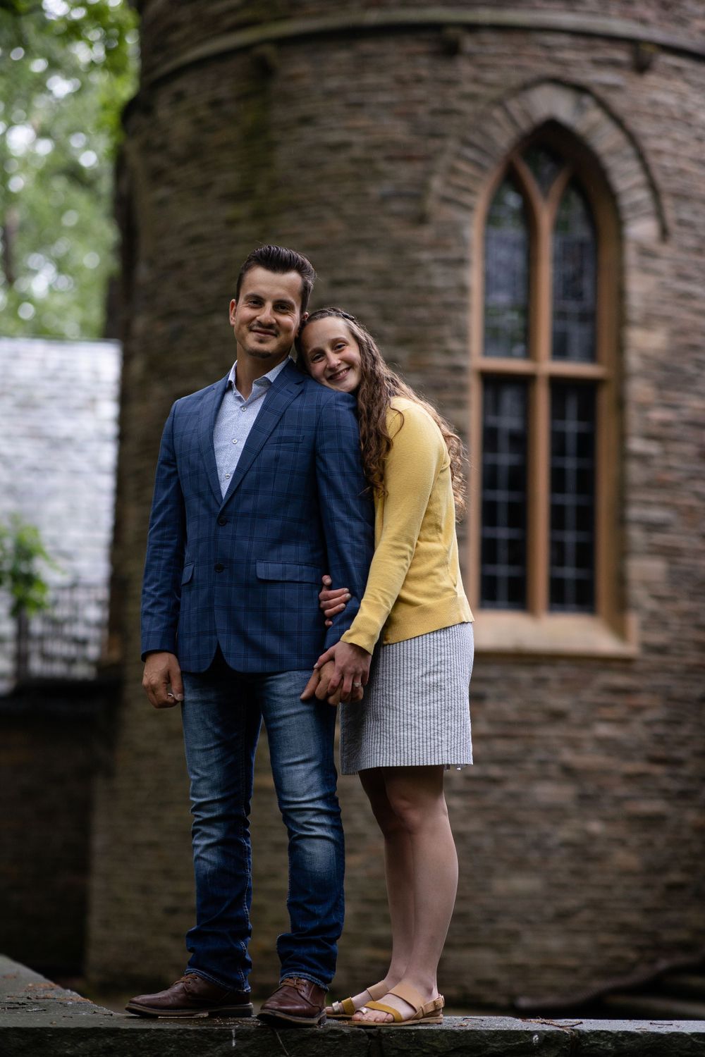 Couple in coordinated yellow and navy outfits pose together against stone castle architecture.
