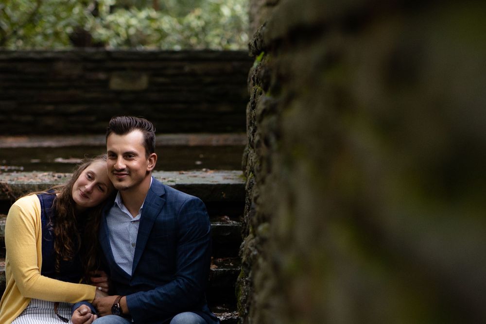 Couple in yellow and blue share a tender moment on stone steps surrounded by nature.