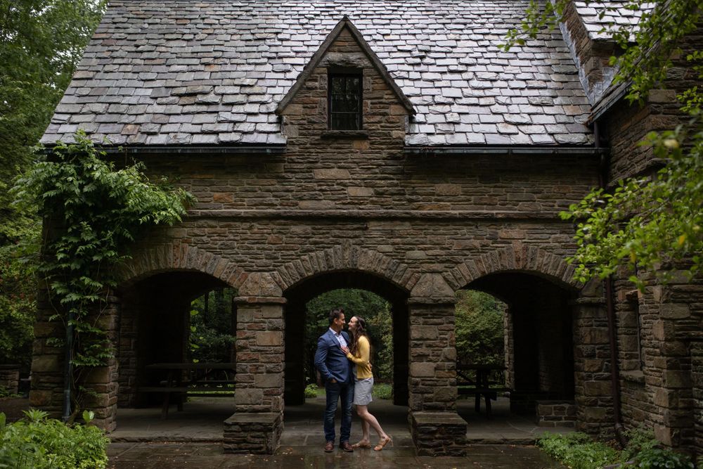 Couple embracing under stone archway of historic building with gothic architecture.