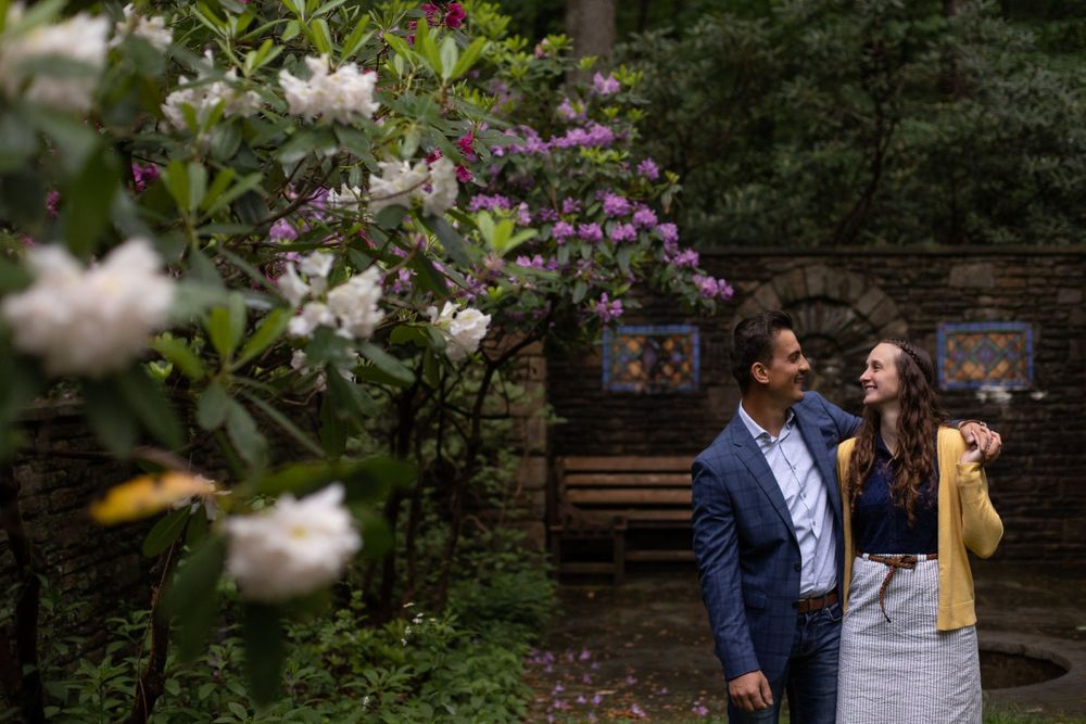 A couple sharing a tender moment in a lush garden with white flowers and a rustic bench.