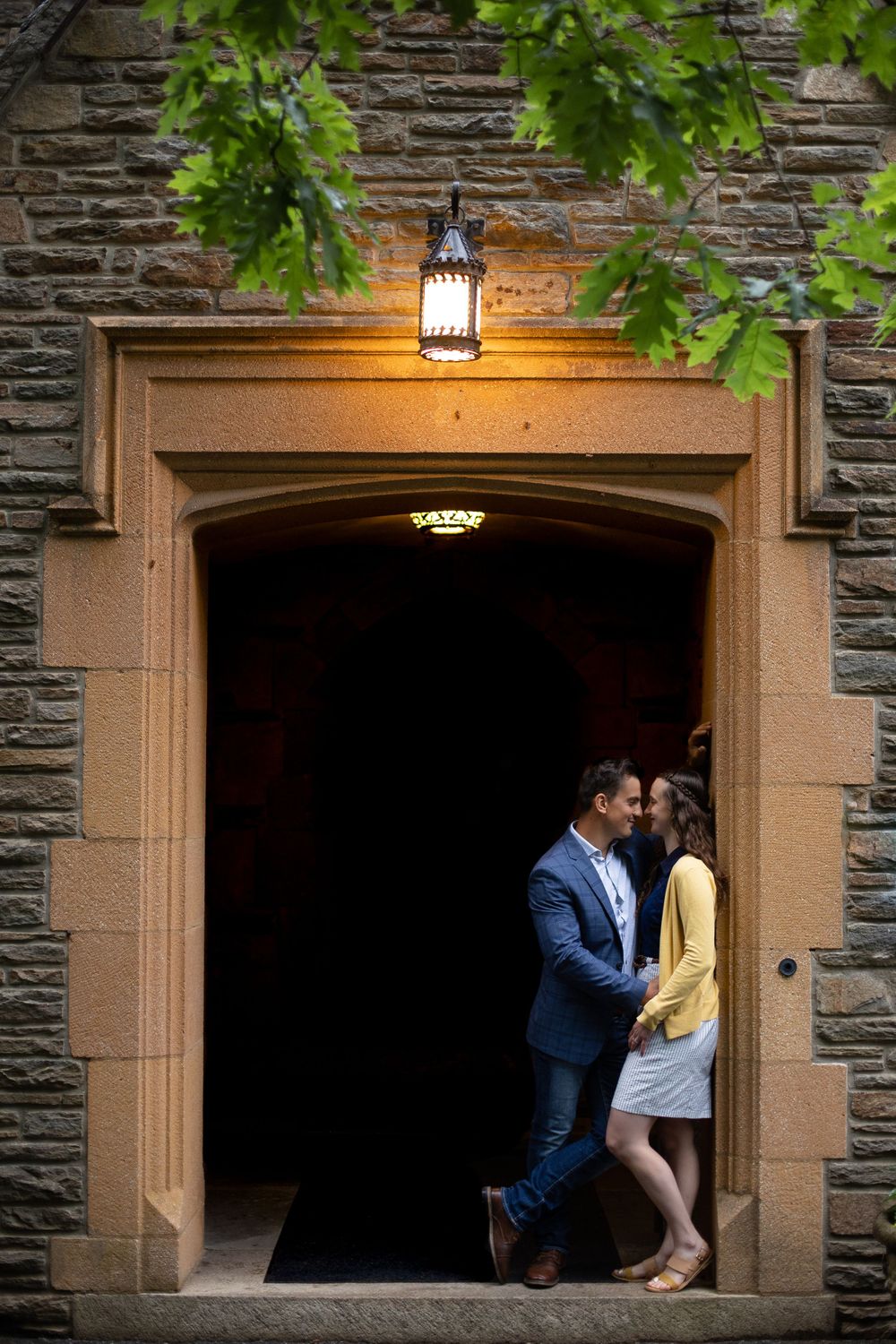 A couple embracing in a stone archway illuminated by a hanging lantern at dusk.