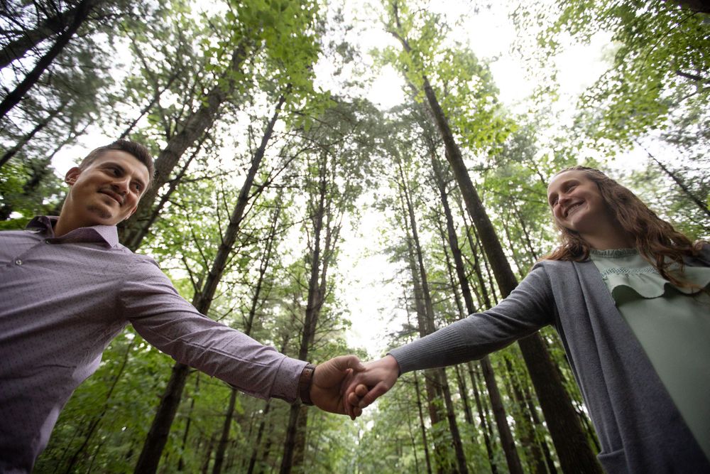 Two people joining hands in a forest with tall trees reaching skyward.