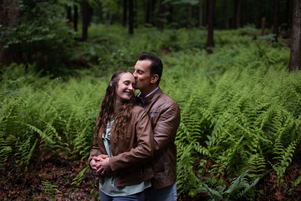 A couple sharing a joyful moment surrounded by ferns in a misty forest.