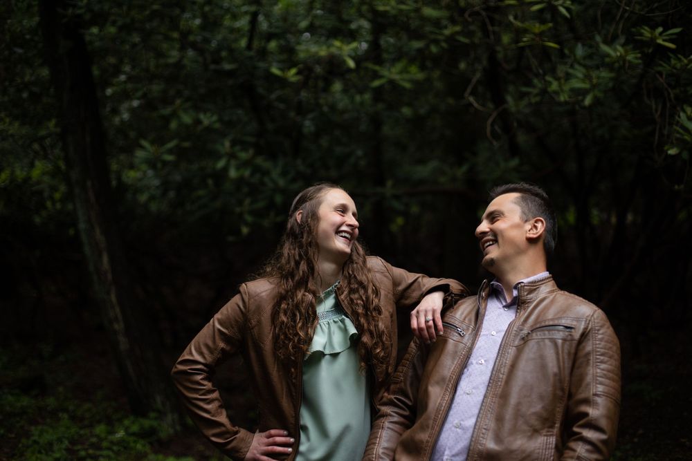 Joyful couple laughing together in a moody forest setting.