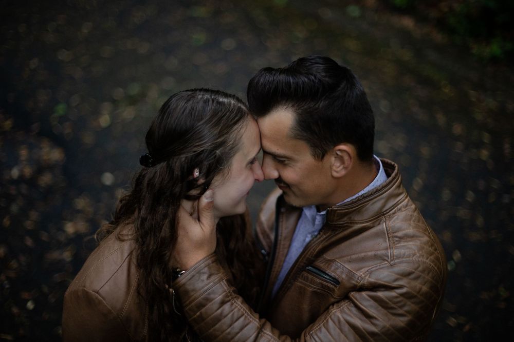 Intimate moment shared between a couple in matching brown jackets during a forest photoshoot.