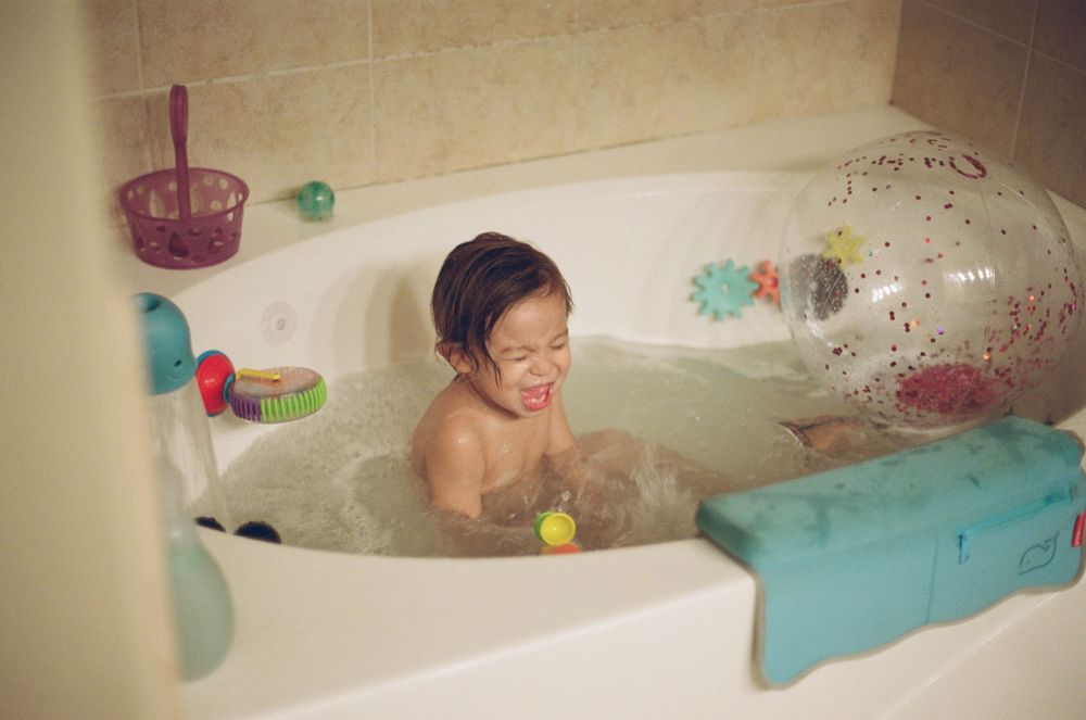 A bathroom scene with colorful bath toys and bubbles floating in the tub.