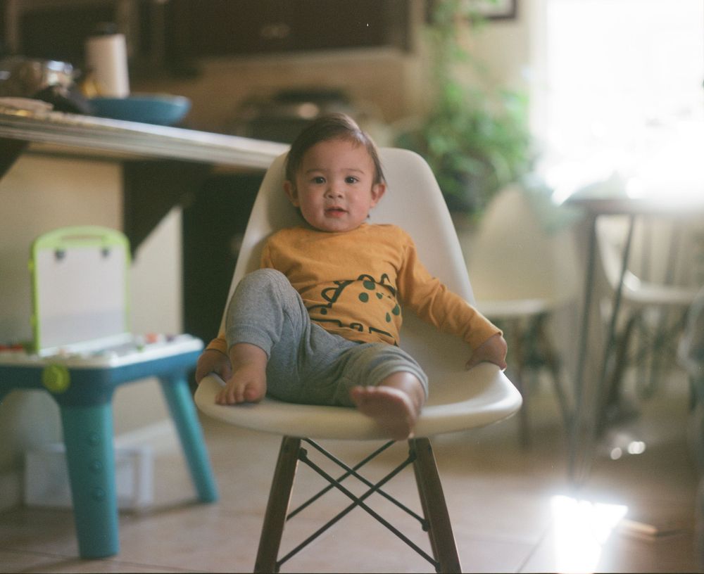 A child sits in a modern white chair in a naturally lit room.