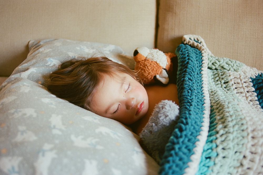 Small child sleeping peacefully under a teal and white crocheted blanket.