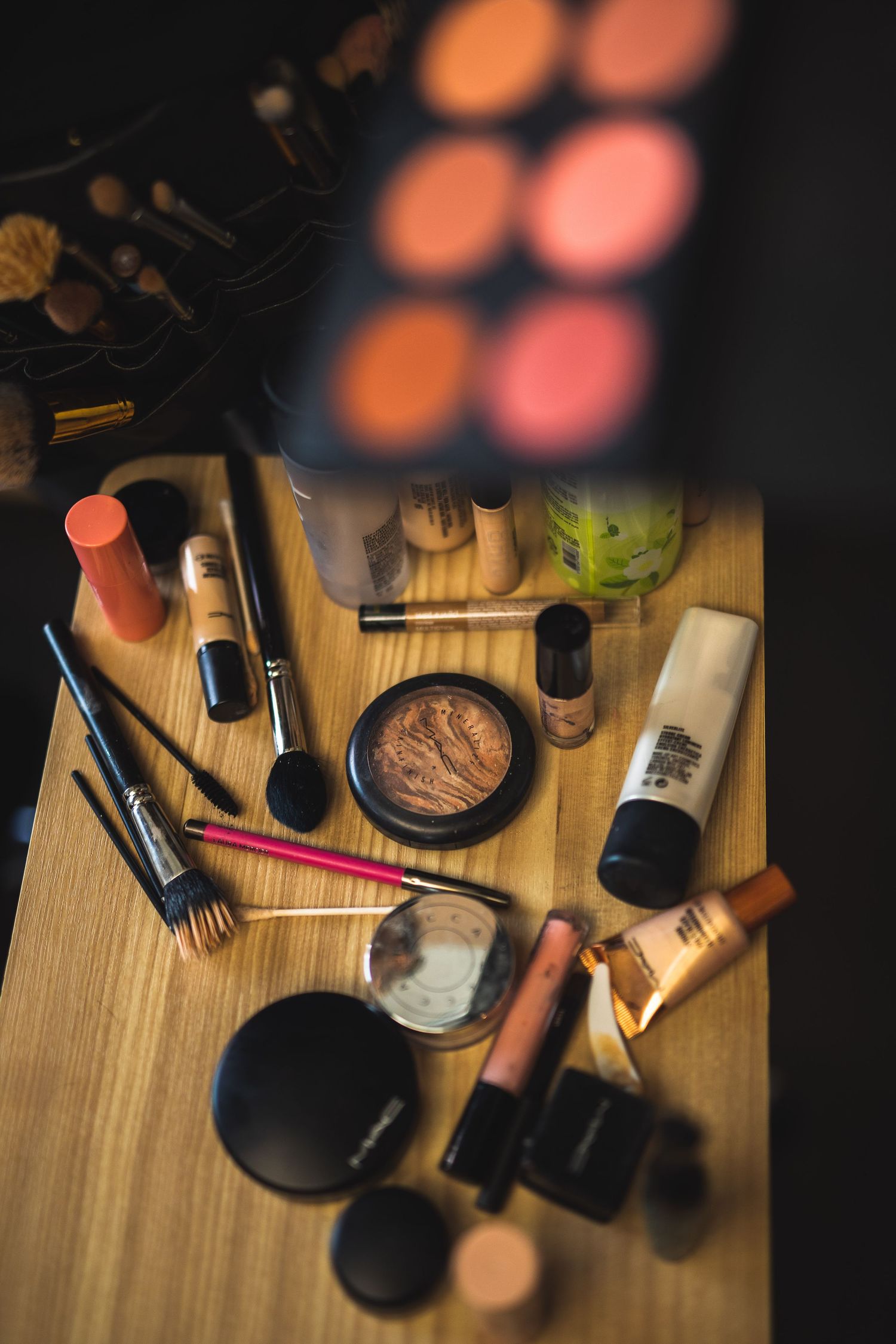 Overhead view of various makeup products and cosmetics scattered on a wooden surface.