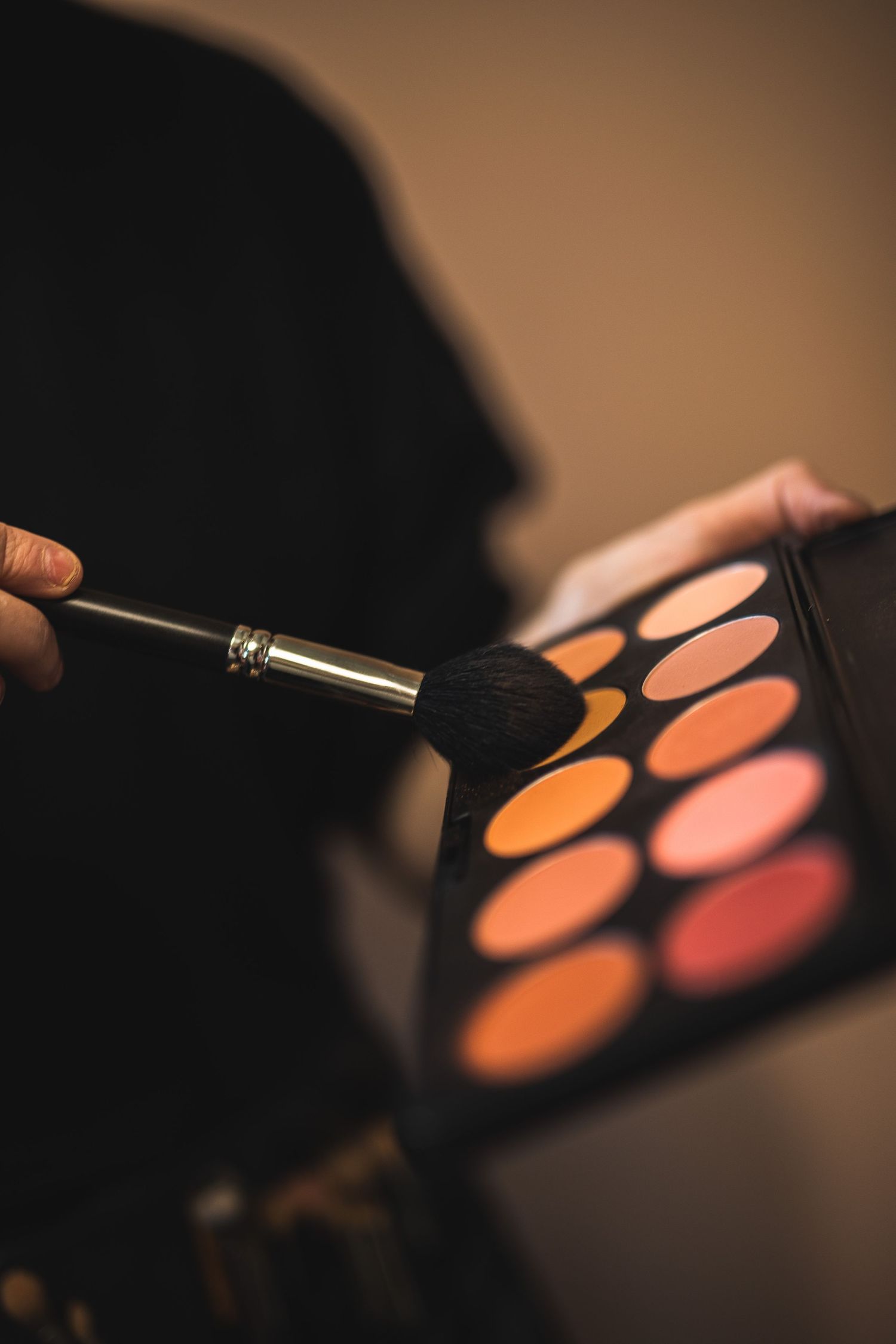 Close-up of a makeup brush selecting color from an orange and pink eyeshadow palette.