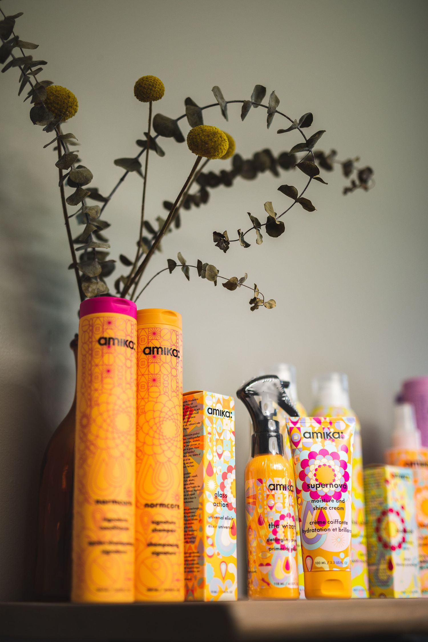 Amika hair products in orange bottles displayed with dried flowers in a decorative arrangement.