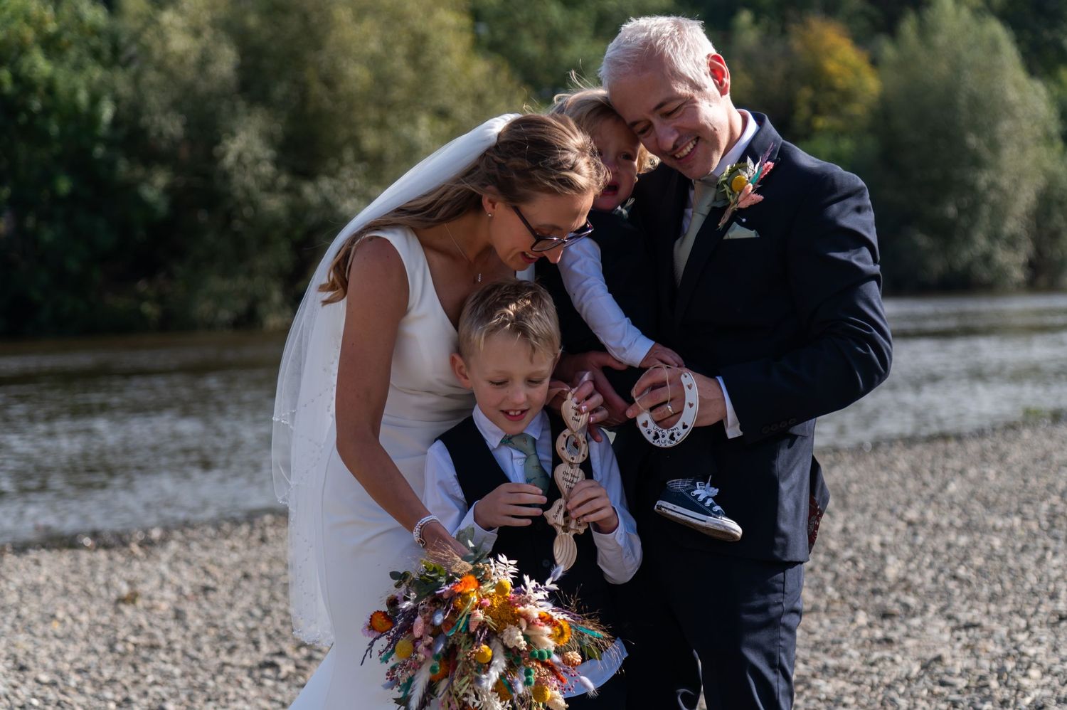 Wedding party shares intimate moments together on a rocky shore near a tranquil lake.