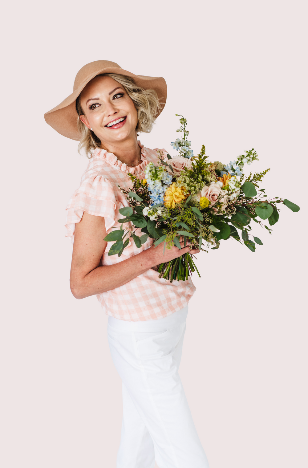 Stylish woman in floppy hat and polka dot blouse holding colorful wildflower bouquet.