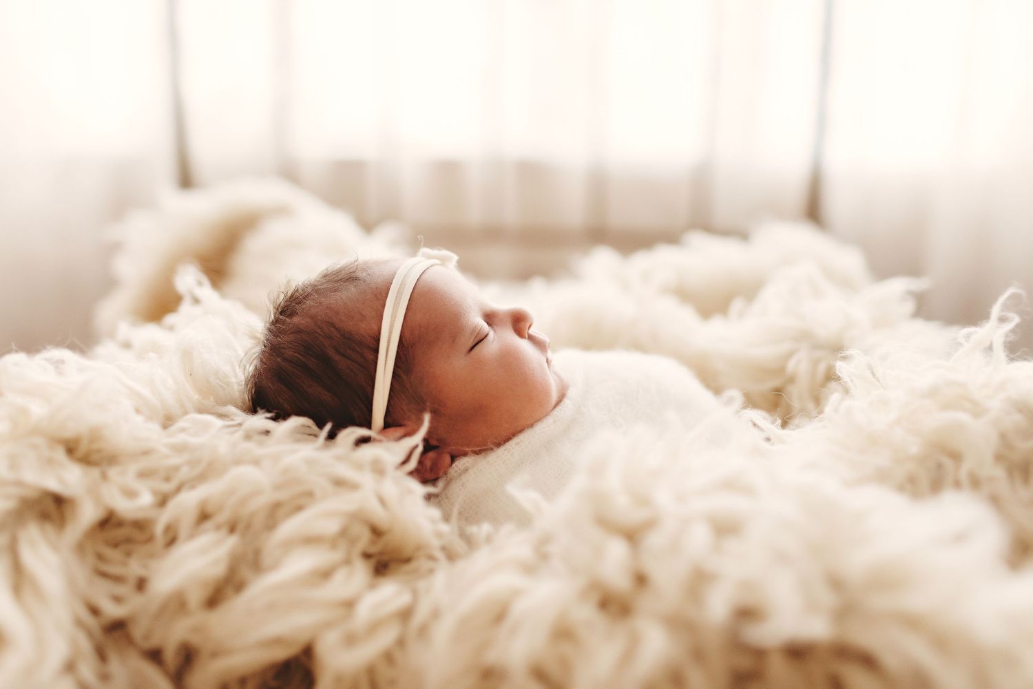 Peaceful newborn baby sleeping on soft cream colored fur blanket.