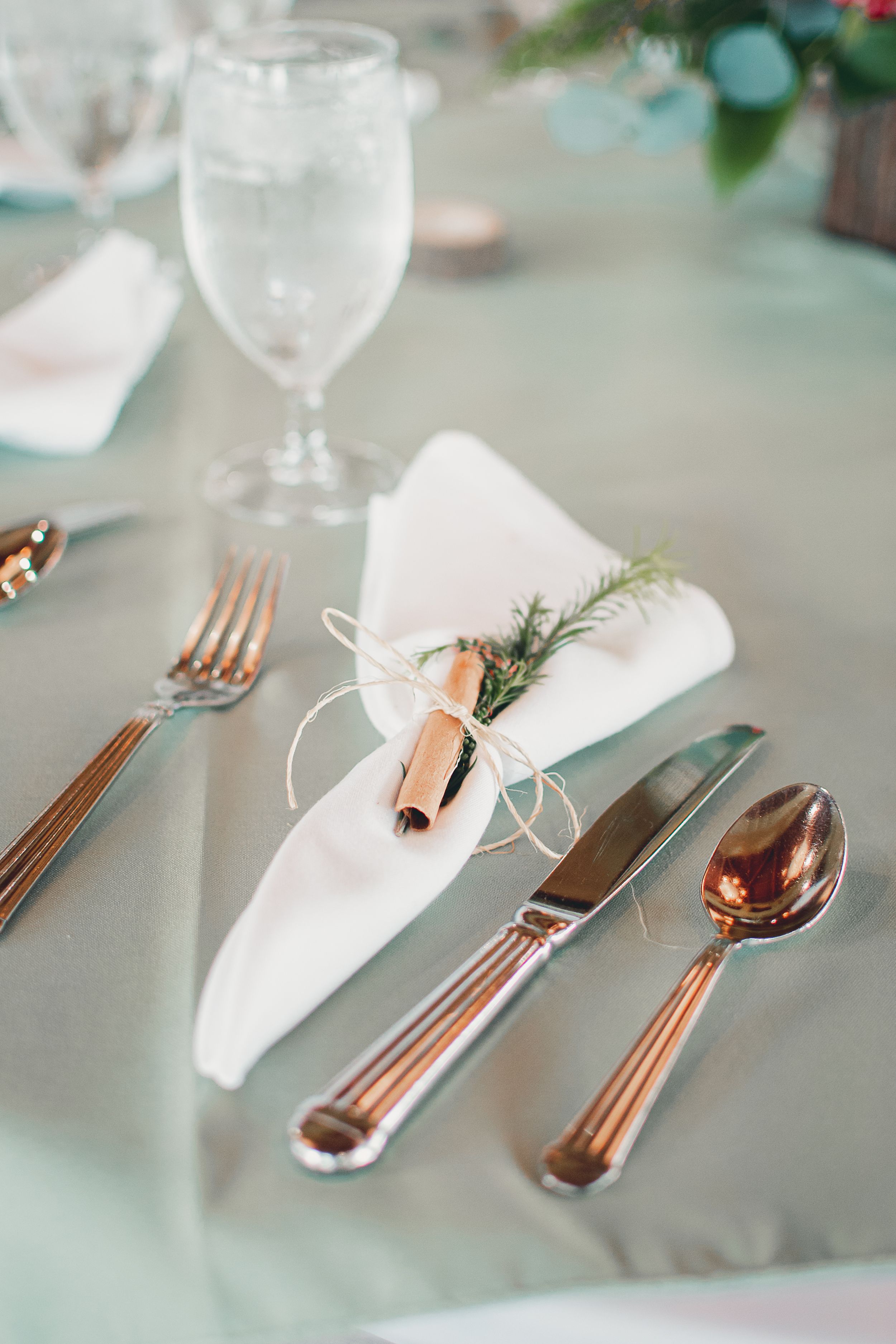Elegant place setting with rose gold cutlery and white napkin with herb sprig.