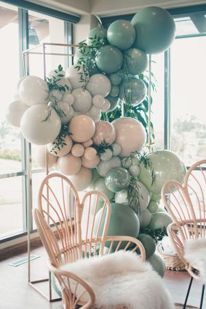 Modern baby shower decor featuring a stunning balloon arch in soft mint and white with greenery accents.
