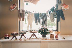 Baby shower dessert table with hanging clothesline display of baby clothes and cupcake stands.