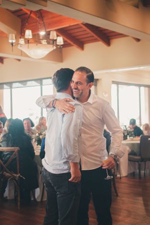 Two people sharing a warm embrace at an indoor event with elegant lighting and wooden beams.