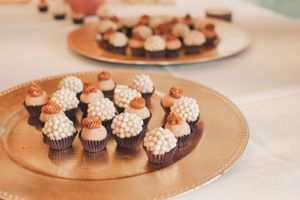 Chocolate cupcakes decorated with white frosting and orange toppers displayed on gold plates.