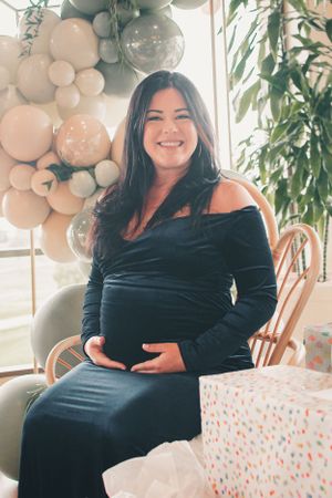 Maternity celebration with balloon arch and presents featuring woman in black velvet dress.