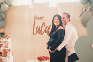 Elegant baby shower setup with balloon arch and 'Baby Luca' sign in warm lighting.