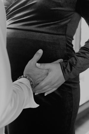 Black and white photo of hands tenderly placed on pregnant belly in intimate moment.