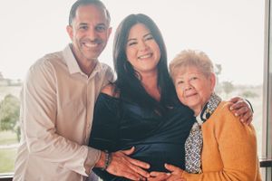 Three generations pose together at baby shower celebration with scenic window view.