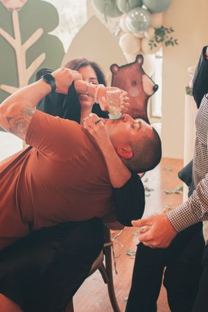 Guests playfully sharing drinks at a celebratory party with decorative elements in background.
