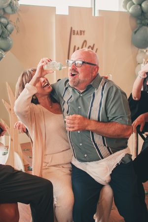 Couple sharing laughter while drinking at a baby-themed celebration event.