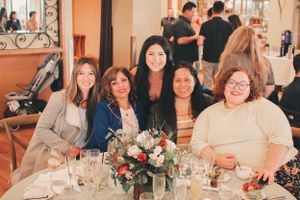 Group photo around dining table with floral centerpiece at celebration event.
