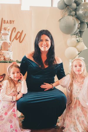 Expectant mother in navy dress poses with children at baby shower celebration.