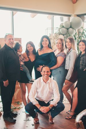 Group photo at baby shower featuring balloon arch and modern decor elements.