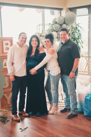Group of people standing together at a celebration in a room with hardwood floors and white balloons.