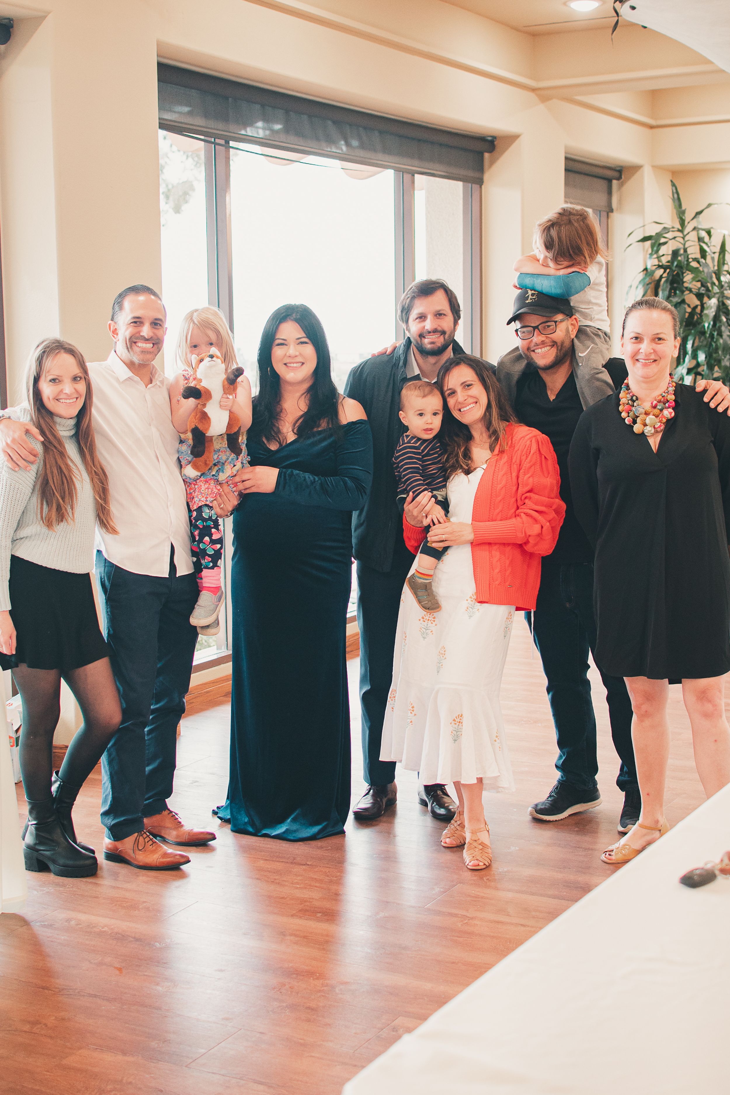 A group of people gathered together in a bright room with hardwood floors for a casual family gathering.
