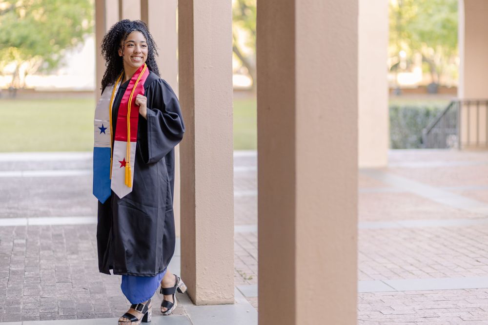 Graduate in academic regalia walks through campus colonnade during graduation photo session.