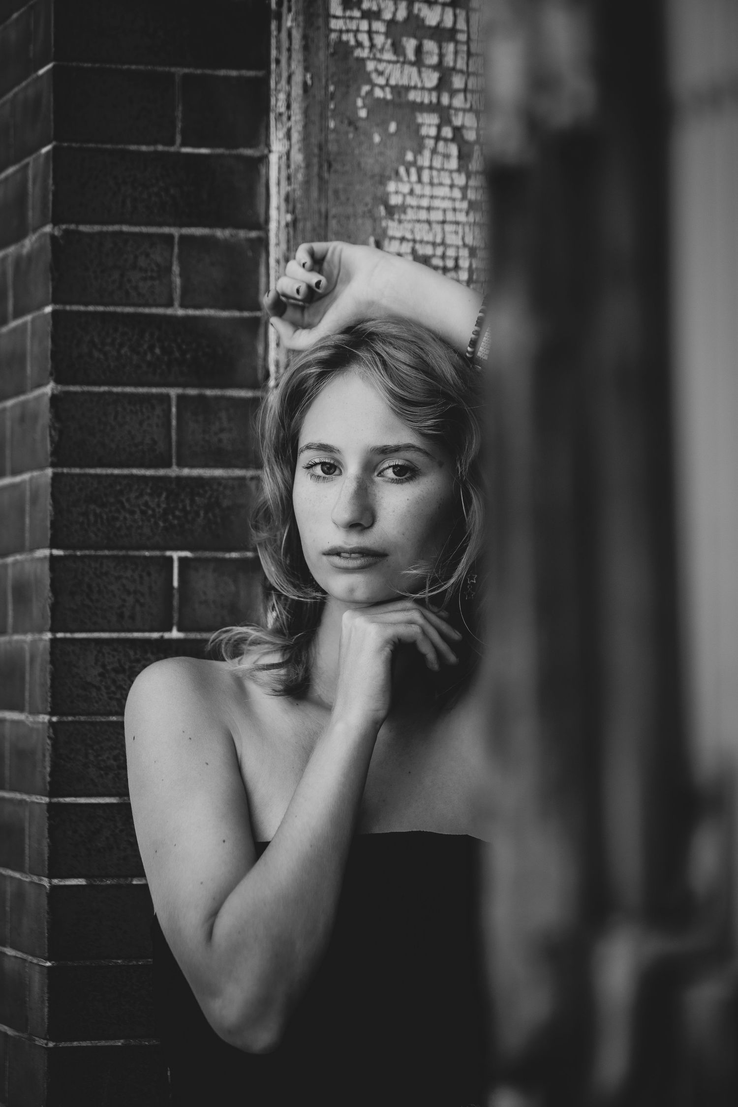 Black and white portrait against brick wall with dramatic lighting and classic pose.