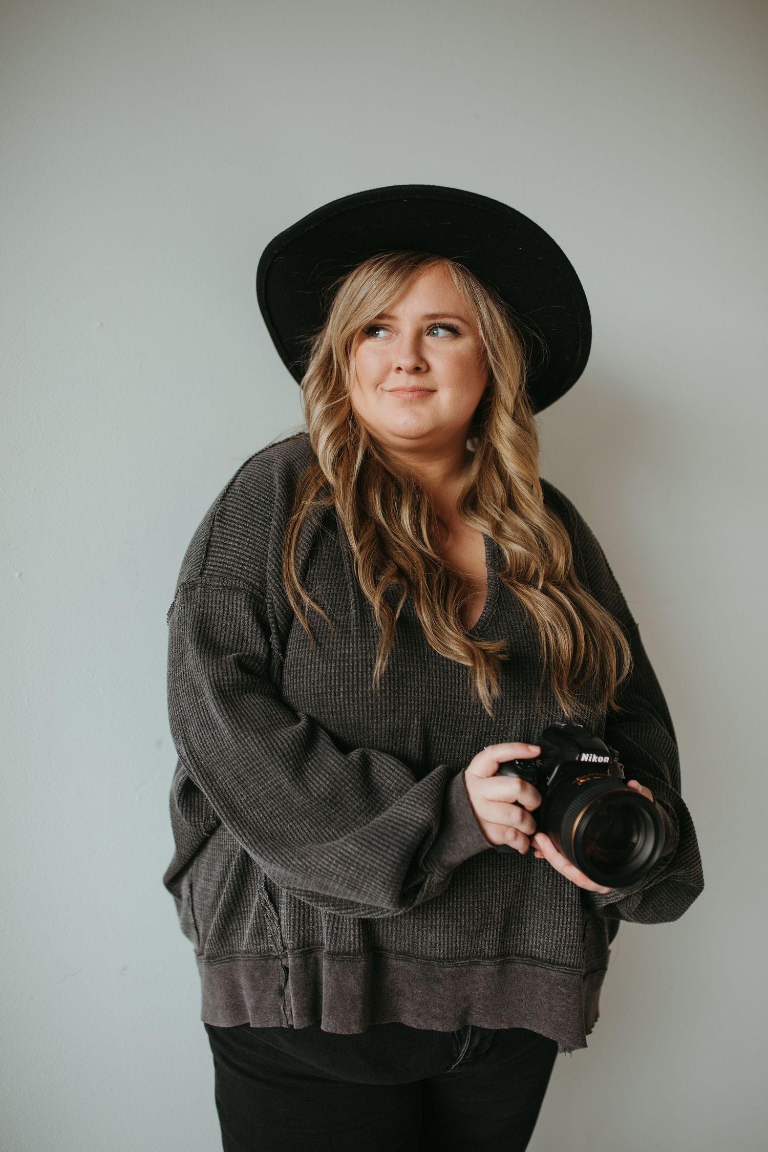 Creative portrait series with black hat and gray sweater against white wall.