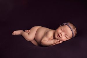 Sleeping newborn with headband posed on dark purple backdrop in artistic style.