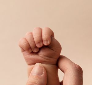 Close-up of tiny newborn baby's fist against peachy background.