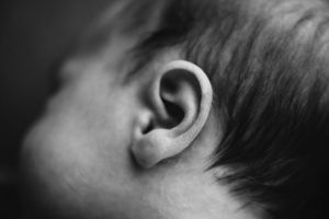 Close-up black and white photograph of a baby's ear and hair.