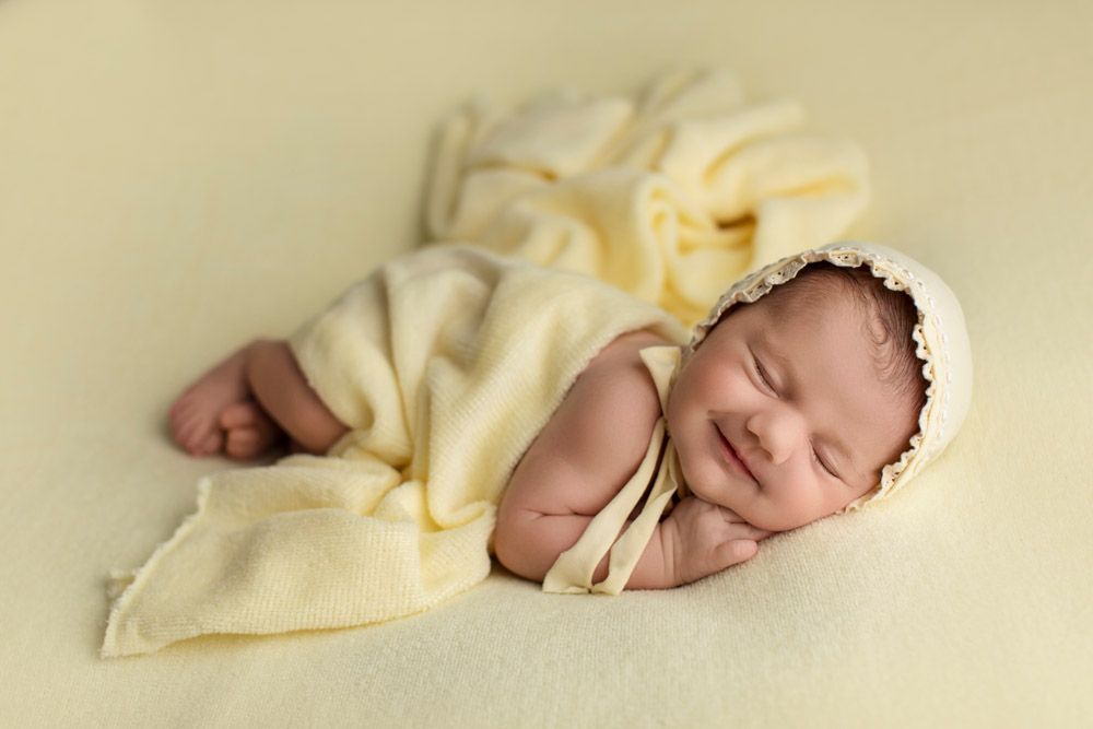Peaceful newborn sleeping under soft yellow blanket against cream background.