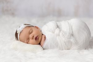 Sleeping newborn in white lace wrap on soft white fur background.