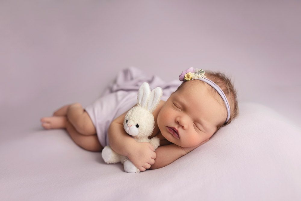 Sleeping baby with plush bunny toy on pink background.