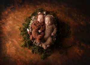 Two newborns in knit outfits nestled in mossy nest with warm lighting.