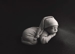 Black and white portrait of sleeping newborn wearing soft white hat.
