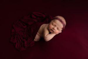 Sleeping newborn with headband against deep red background with fabric draping.