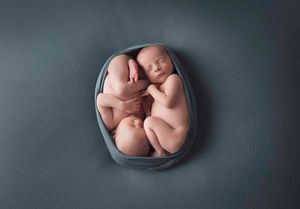 Newborn baby curled up sleeping in a grey oval basket against dark background.