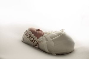 Sleeping newborn wrapped in white fabric with delicate lace detail.