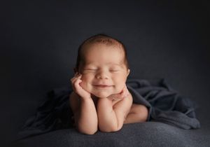 Peaceful newborn resting on grey blanket with hands propped under chin.